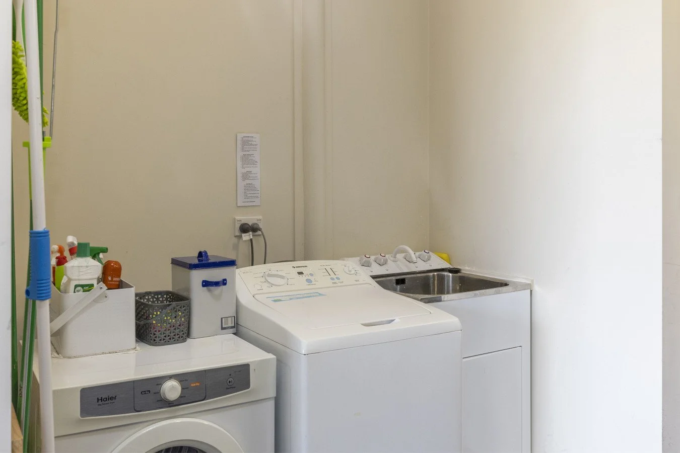 Laundry room with washing machine, utility sink, and shelves with cleaning supplies.