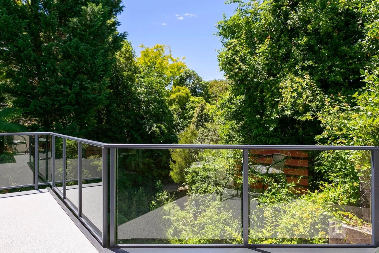 View from a balcony looking out at lush green trees and a clear blue sky.