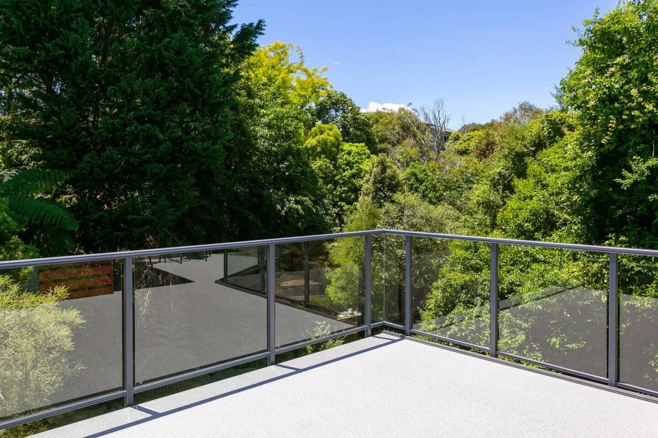 Balcony with glass railing overlooking lush green trees and blue sky