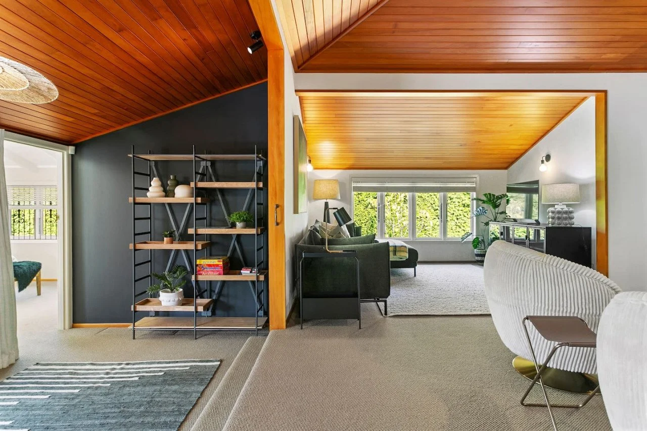Living room with wooden ceiling, black and white walls, large window, modern furniture, and decorative plants.
