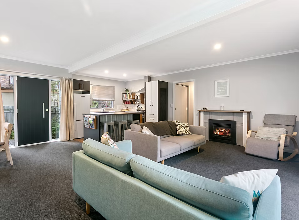Living room with gray sofa, armchair, fireplace, open kitchen area with bar stools, sliding glass door, and neutral decor.