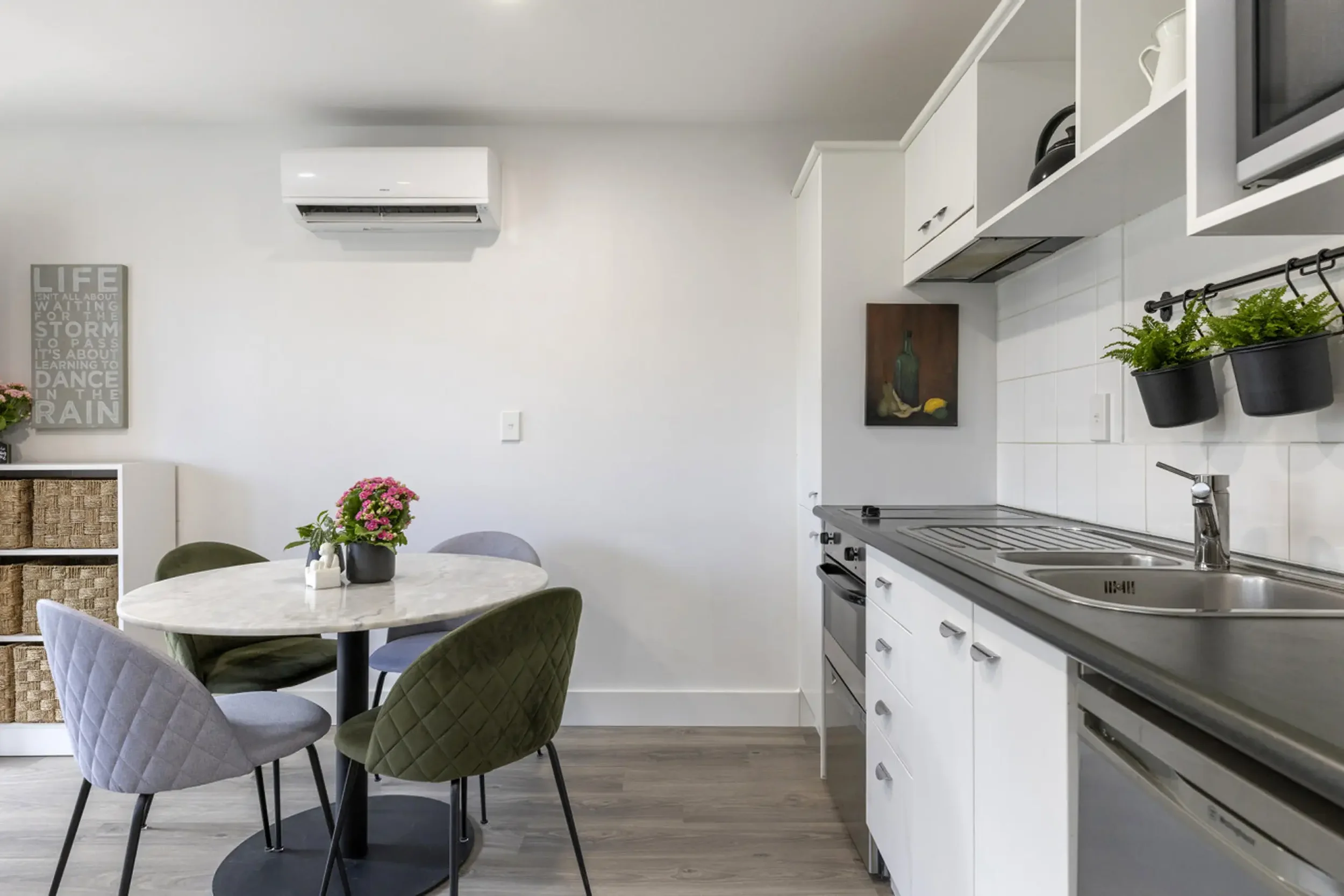 Modern kitchen and dining area with a round table, four quilted chairs, kitchen cabinets, sink, and potted plants.