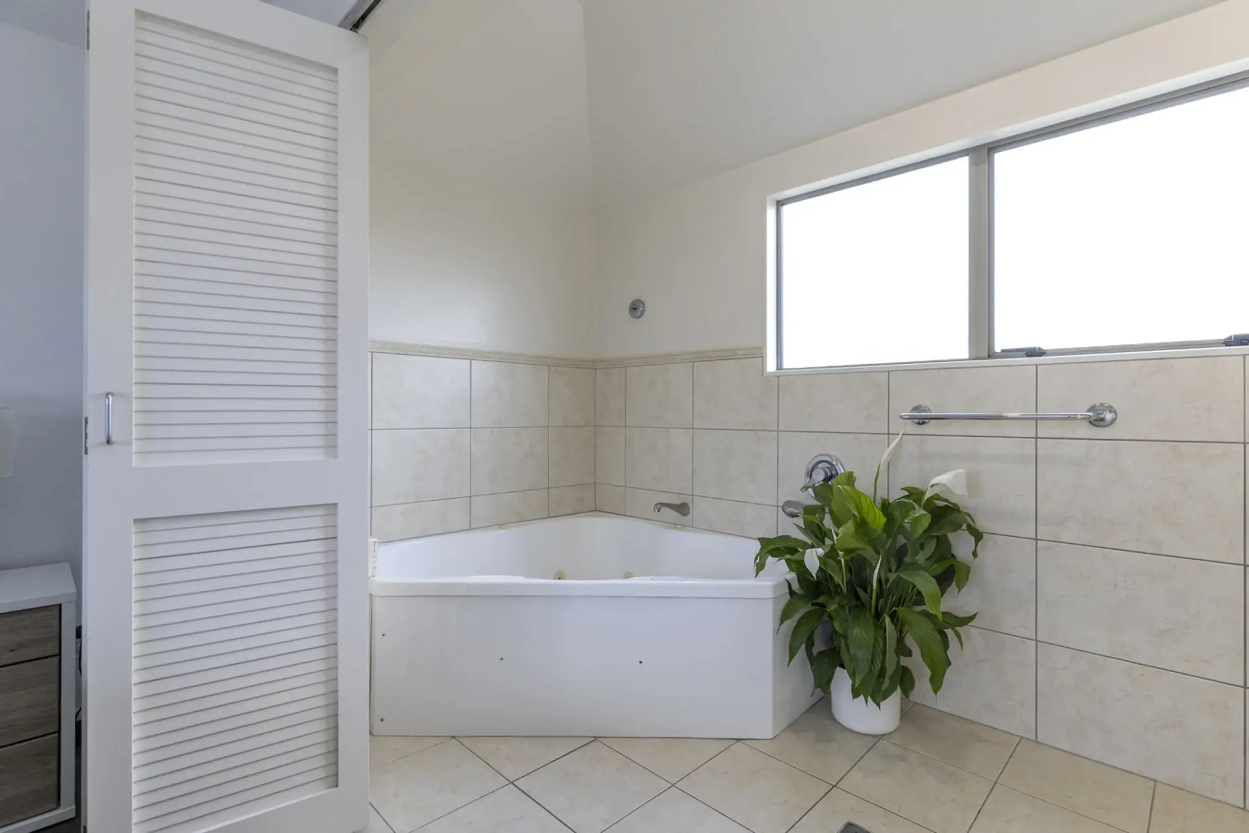 Bathroom with a corner bathtub, a potted plant, and a window on the wall.