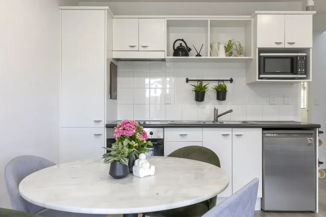 A modern kitchen with white cabinets, a black countertop, and a small dining table with a flower vase and figurine.