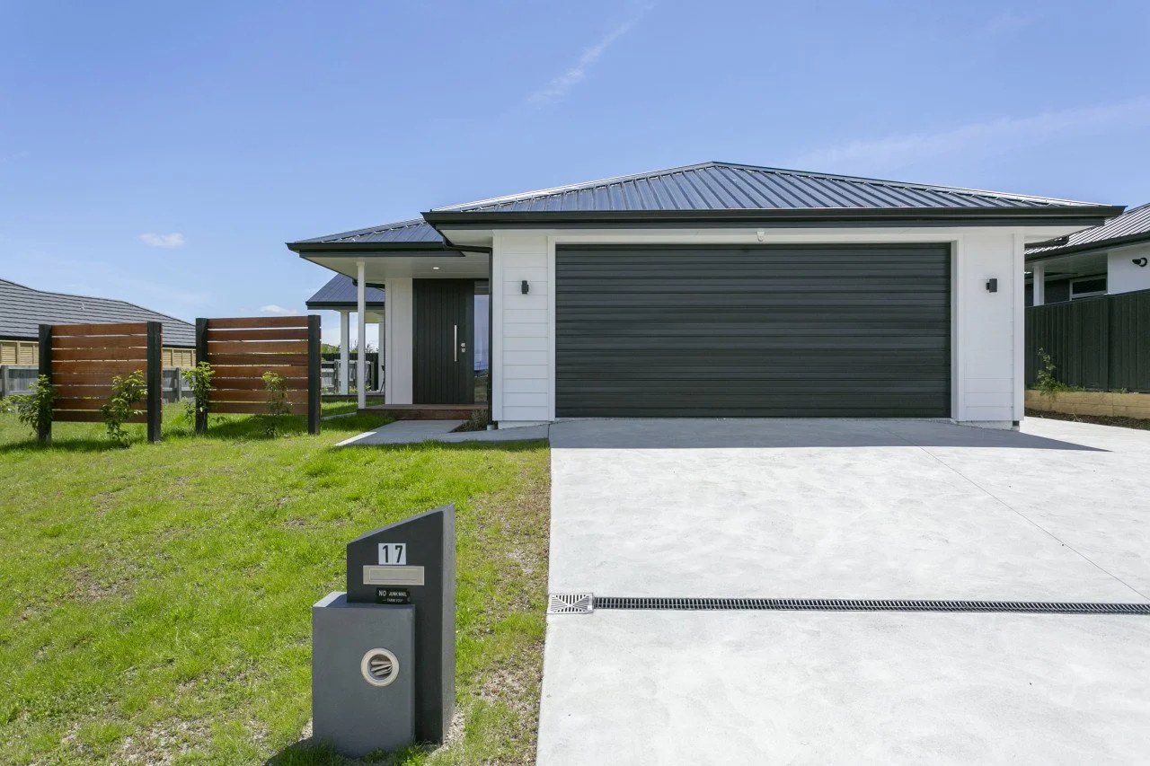 Front view of a modern house with a gray garage door, white exterior walls, small front porch, and a front yard with grass and a gray mailbox marked 17.