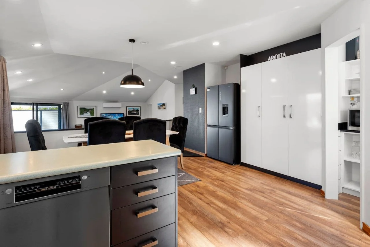 Modern kitchen with white cabinets, black refrigerator, microwave, and dining area with black chairs and artwork on the walls.