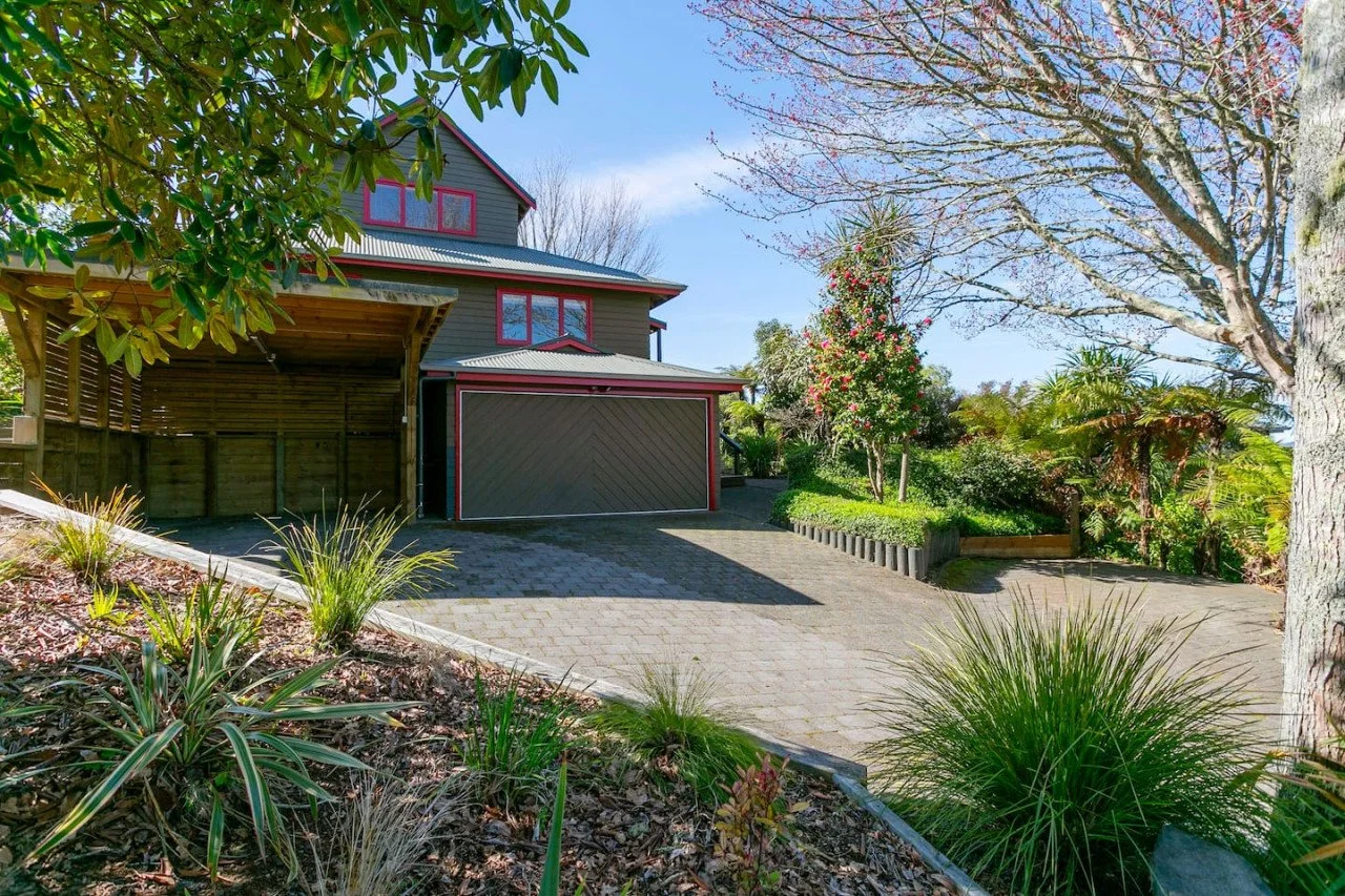 View of a house with a driveway, surrounded by trees and plants, during a sunny day.
