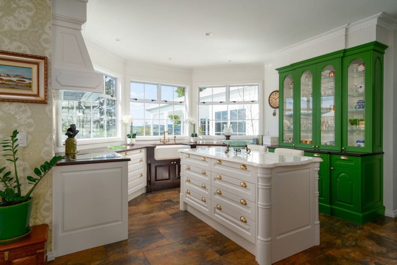 Bright kitchen with white cabinets, a green show cabinet, a white kitchen island, and large windows letting in natural light.