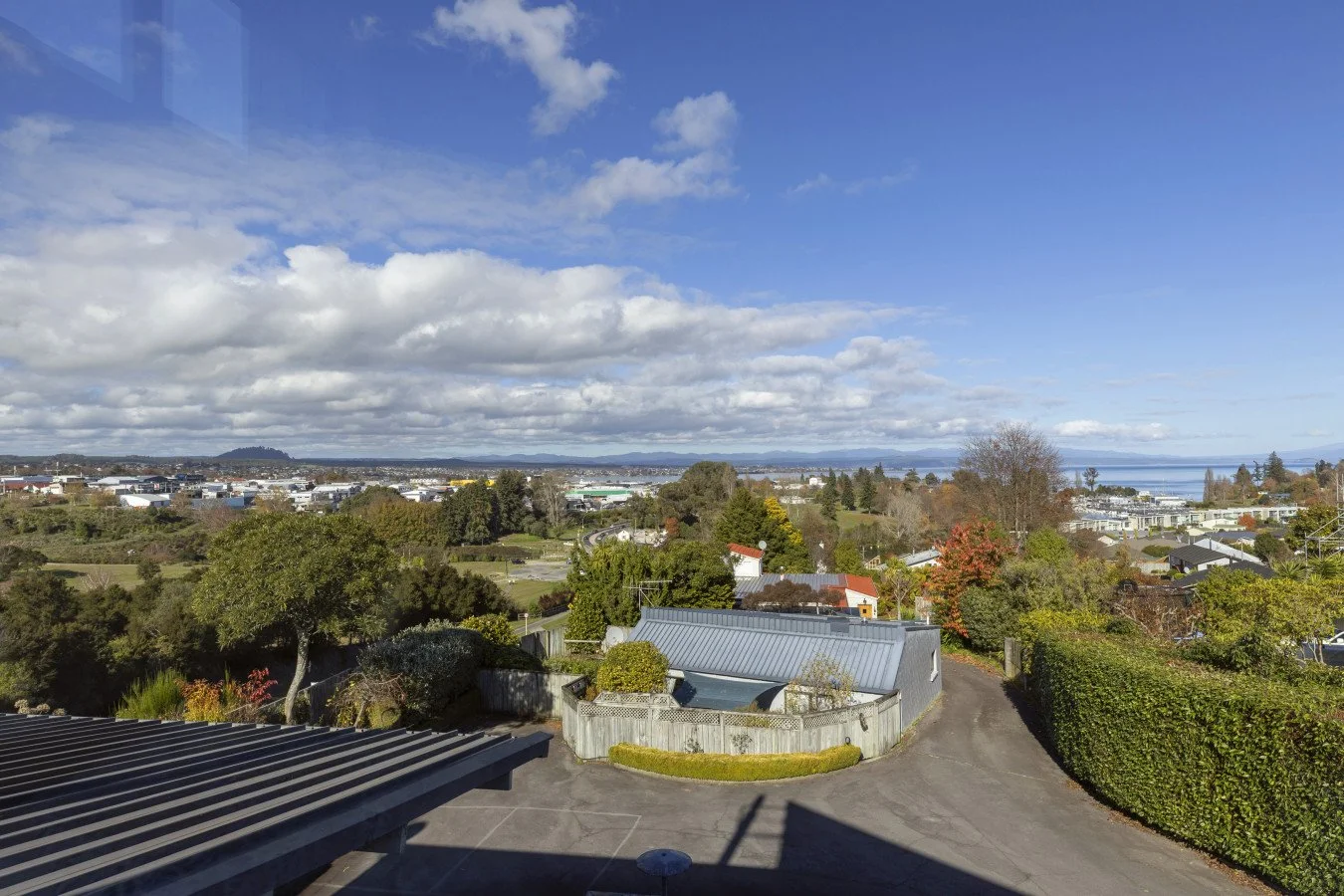 Scenic view of a suburban area with houses, trees, and a distant body of water under a partly cloudy sky.