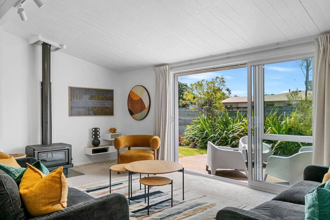 Living room with a sliding glass door opening to a garden patio with outdoor seating, modern decor, and colorful cushions.