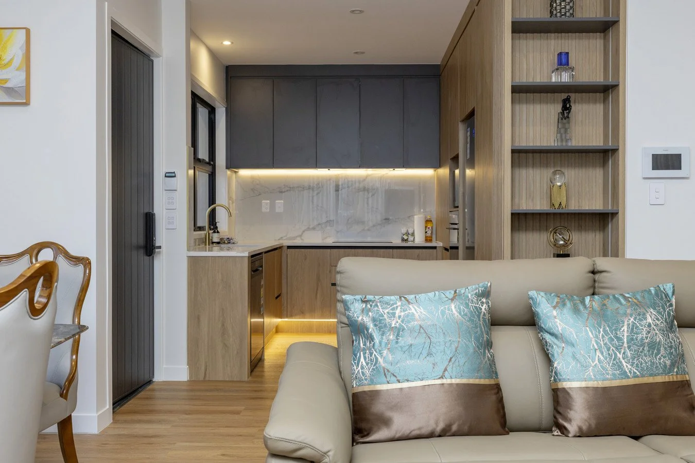 Modern kitchen with gray and wood cabinets, marble backsplash, and a beige sofa with blue and brown pillows in the foreground.