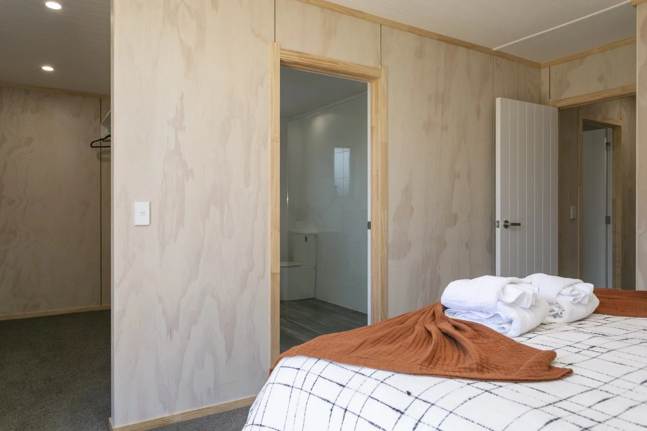 Bedroom with a bed, rolled towels, and a blanket, adjacent to a doorway leading to a bathroom with a toilet.