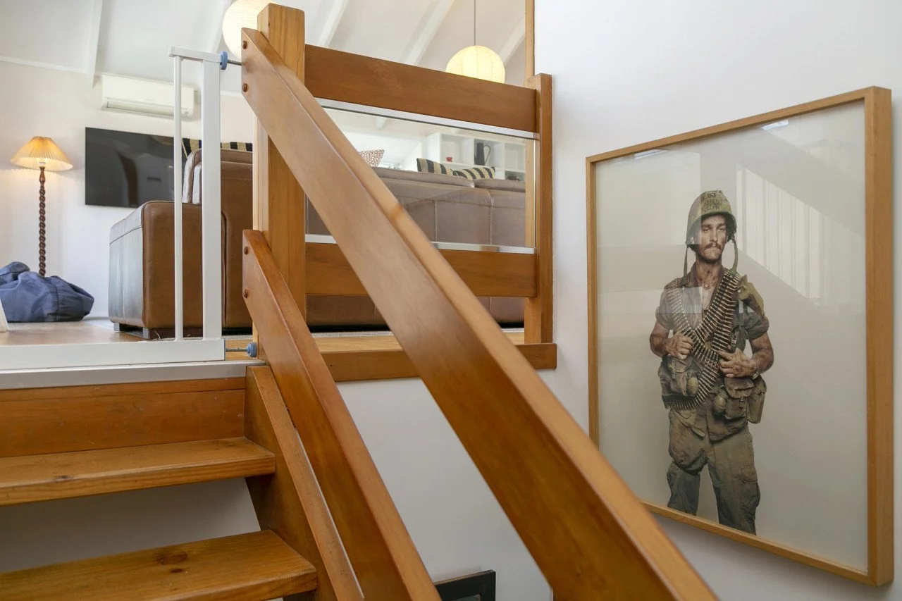 Interior of a house showing wooden stairs, a framed photo of a soldier, a television, and living room furniture.