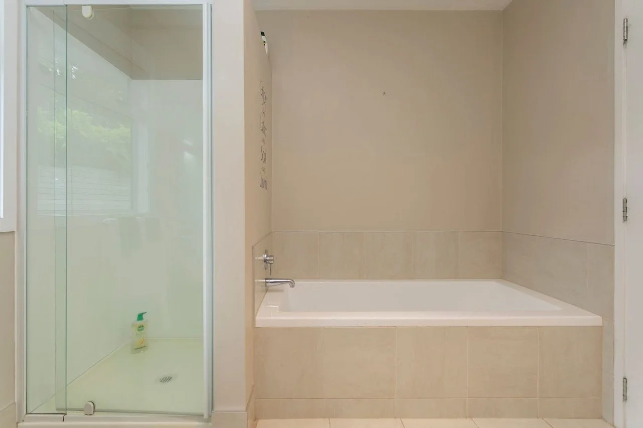A bathroom with a glass shower enclosure on the left and a built-in bathtub on the right, with beige tiled walls and a white door.