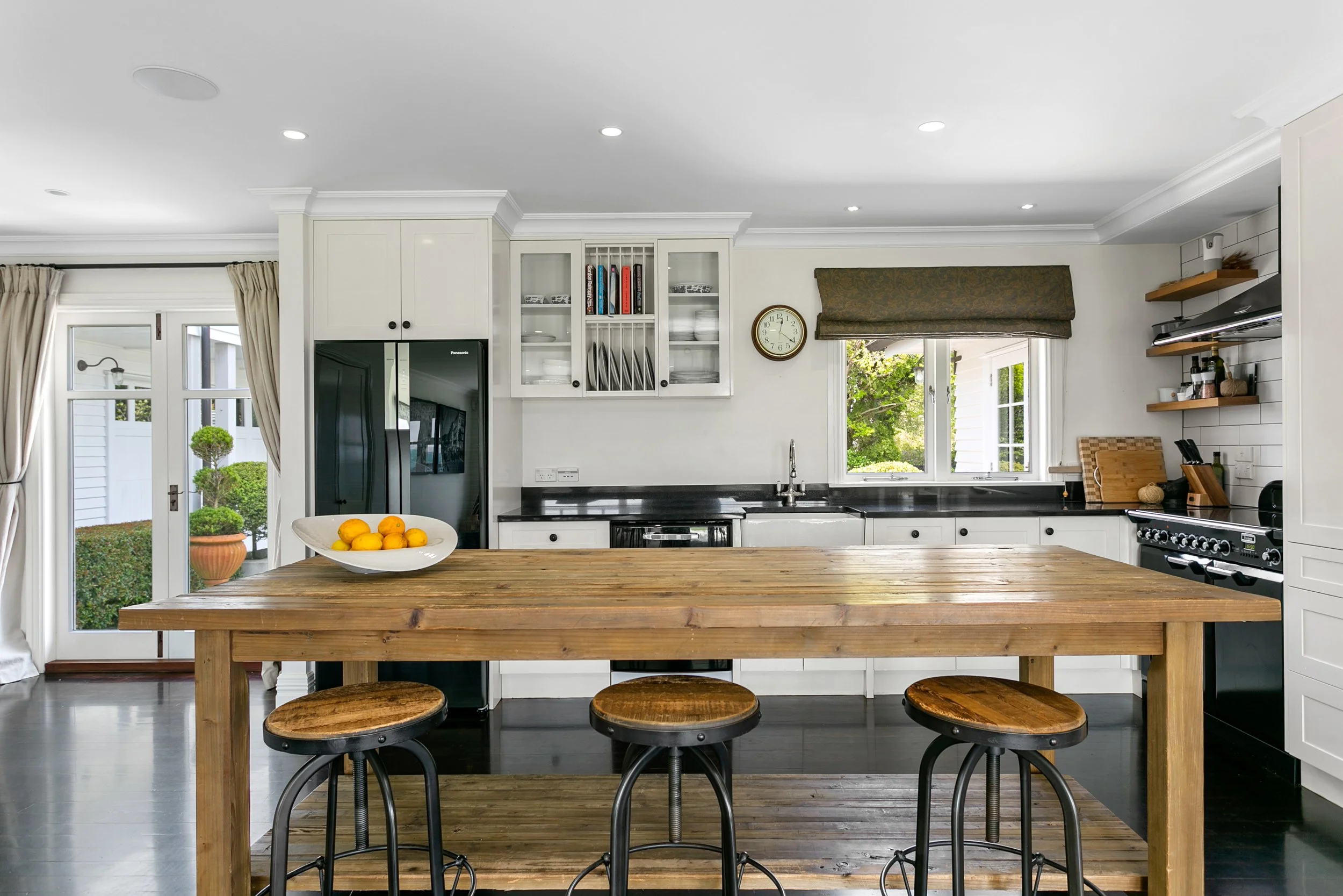 Modern kitchen with white cabinets, black countertops, stainless steel appliances, a wooden island with three stools, and a bowl of lemons on the island.
