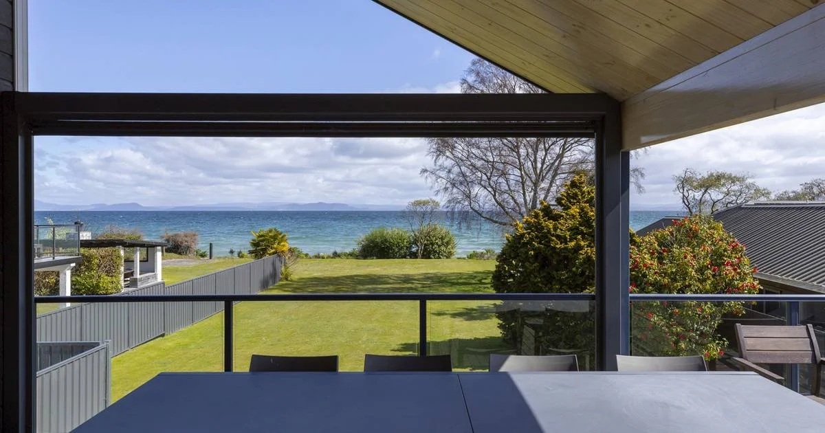 View from a covered porch overlooking a grassy yard with trees and bushes, leading to the ocean with islands in the distance.