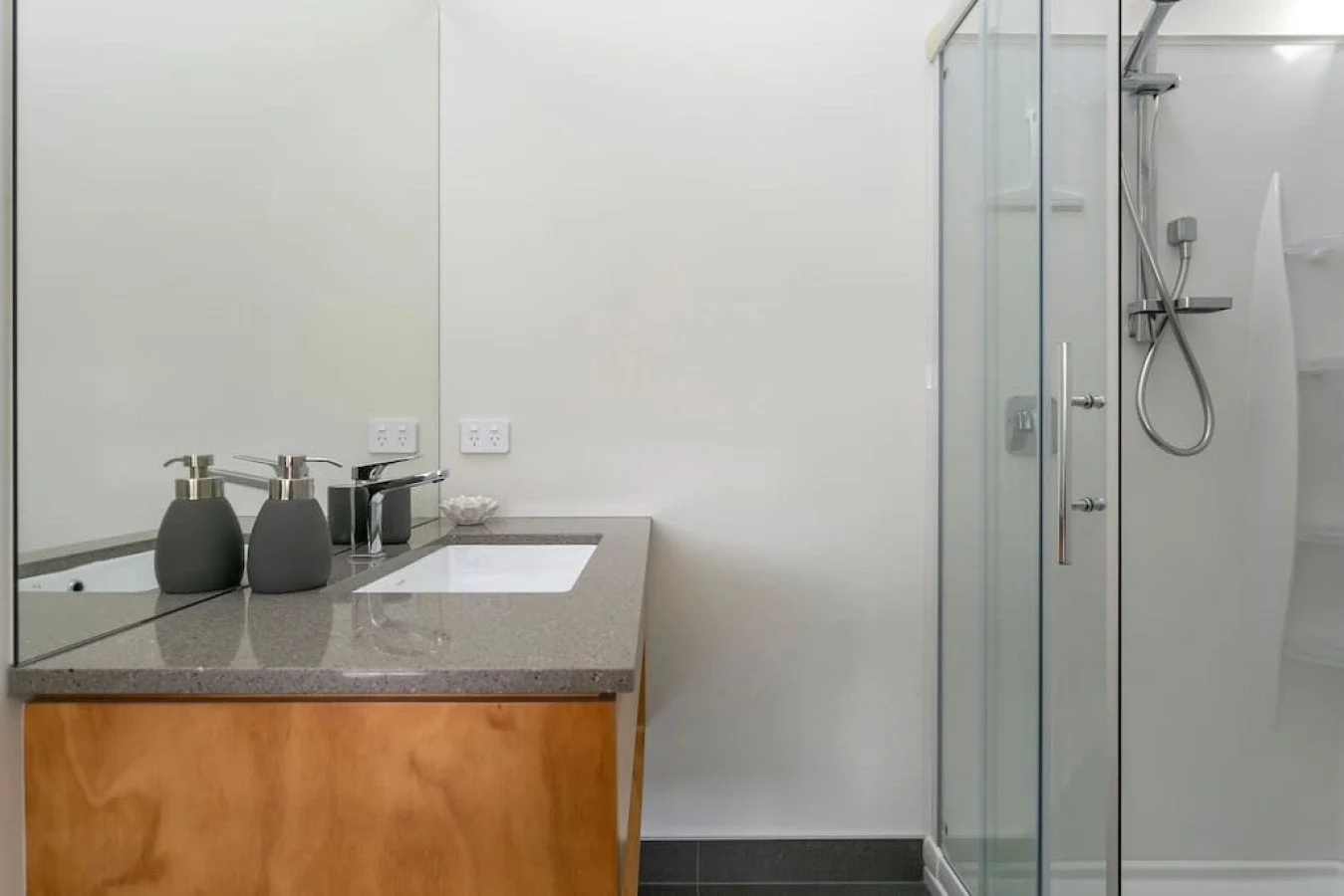 Bathroom with a vanity, soap dispensers, mirror, and a glass shower door.