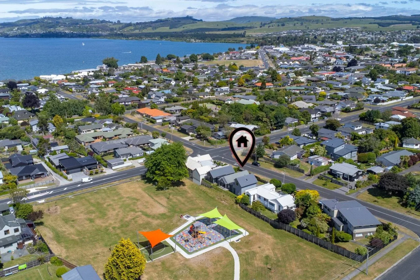 Aerial view of a residential neighborhood near a body of water, with a highlighted house marker and a small park with shaded areas.