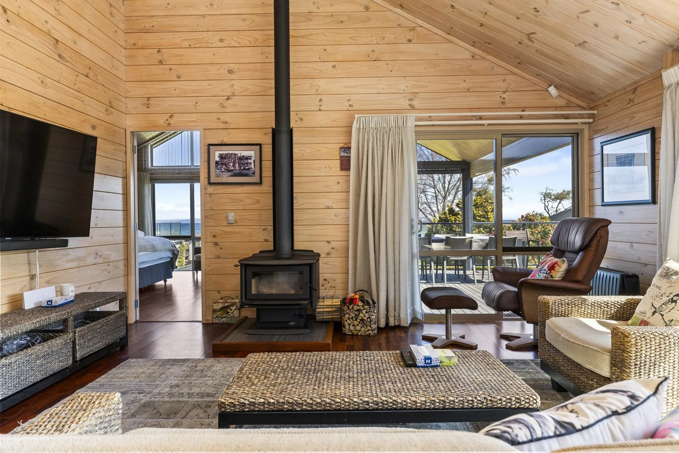 Living room with wooden walls, a black wood stove, a sliding glass door to the patio, and various chairs and a television.