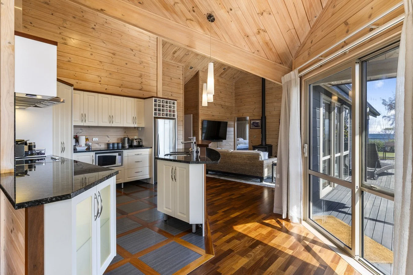 Open-concept kitchen and living area in a wooden cabin with large windows and sliding glass door leading outside.