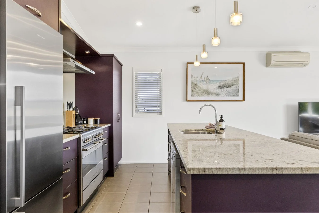 Modern kitchen with purple cabinets, stainless steel appliances, a granite island, and a living area with a picture hanging on the wall.