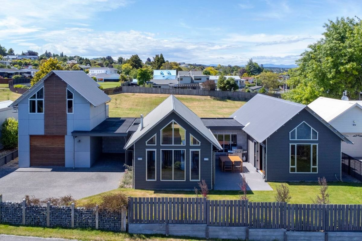 Modern house with gray siding, large front windows, and a backyard patio, surrounded by a wooden fence and neighboring houses.