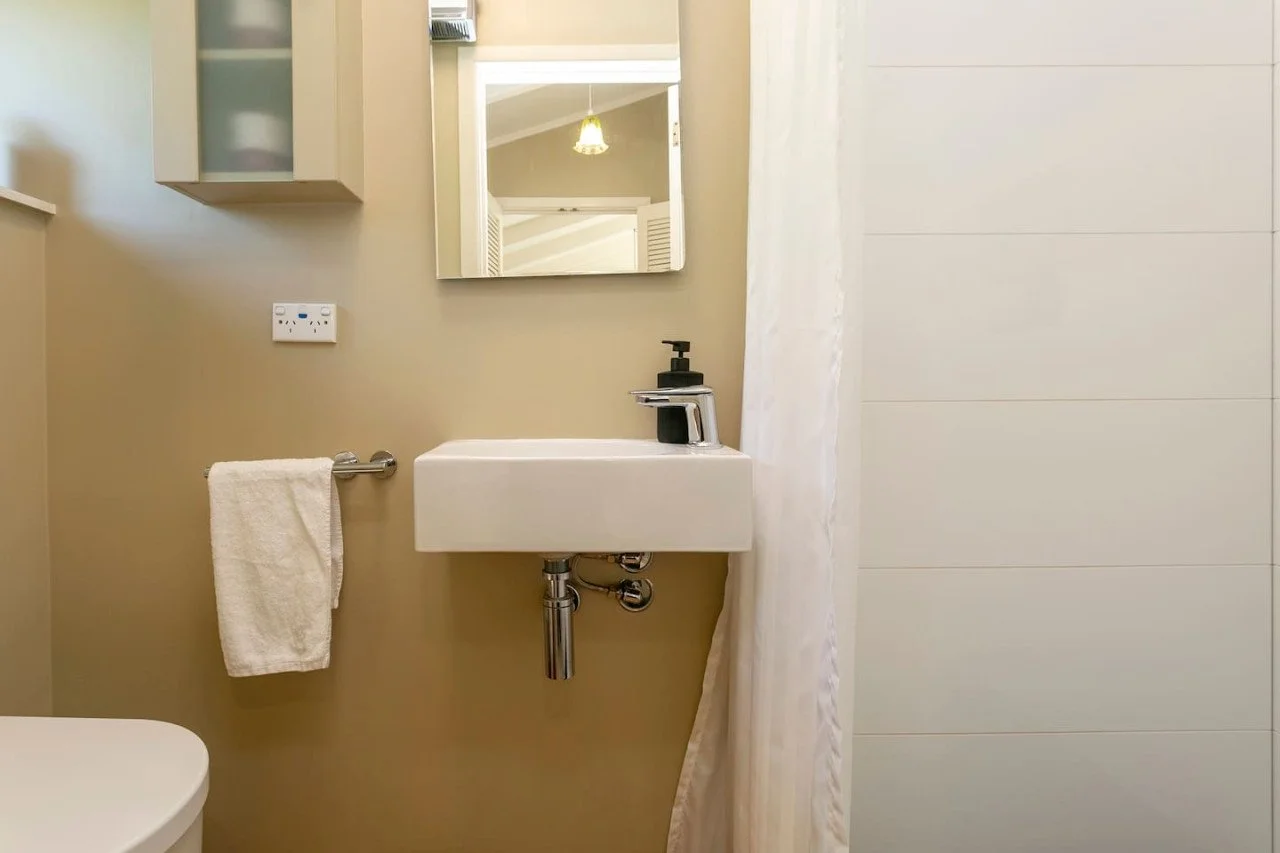 Small bathroom with a wall-mounted sink, mirror, and towel holder, beige walls, and a shower curtain.