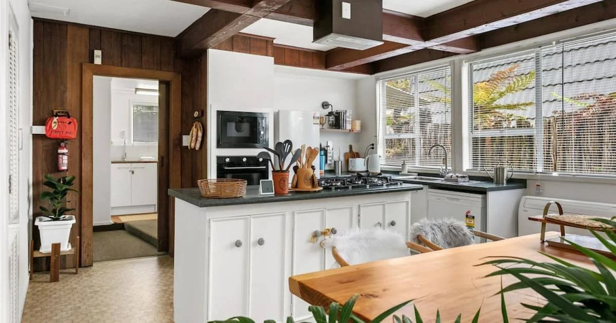 Bright kitchen with white cabinets, black countertops, large windows, and wood-beamed ceiling.
