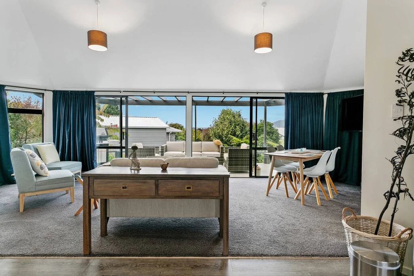 Living room with large glass sliding doors opening to a backyard patio with outdoor seating, blue curtains, and a view of trees and a house outside.