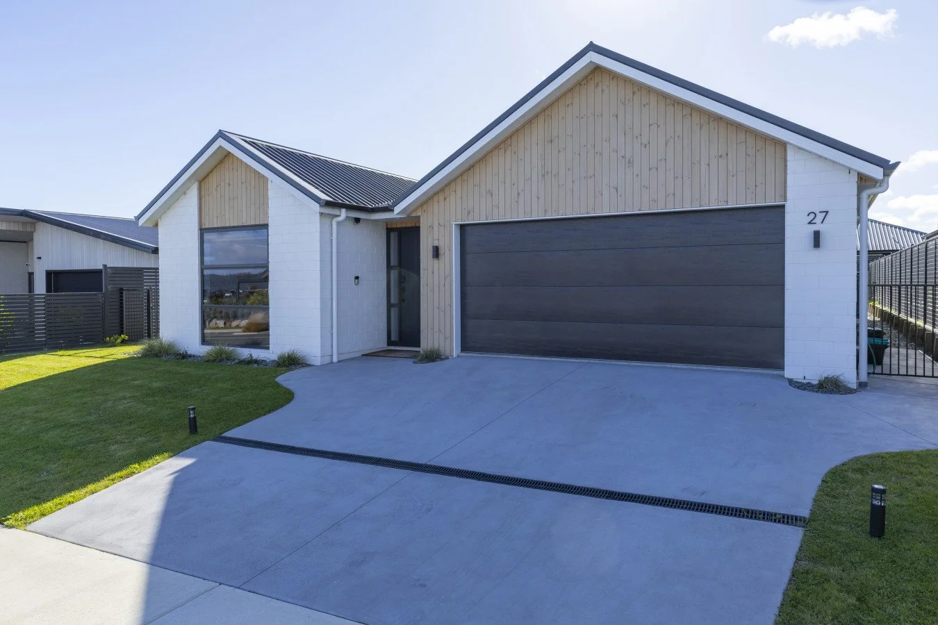 Modern house with a gray garage door, white brick and light wood siding, front yard with grass, and a concrete driveway, under a clear blue sky.