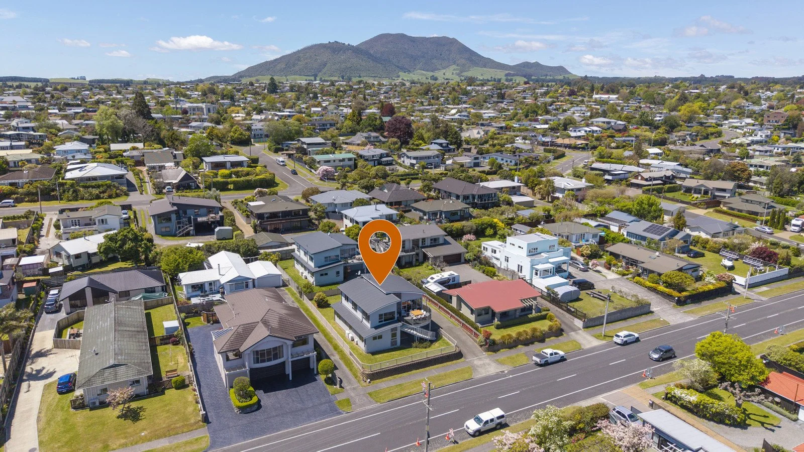 An aerial view of a suburban neighborhood with houses, trees, and streets, with a mountain in the background.