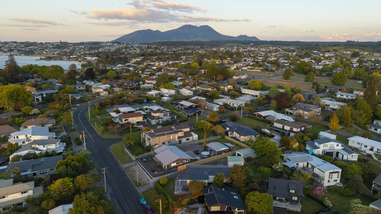 Aerial view of a suburban neighborhood with houses, trees, roads, and a mountain in the background.
