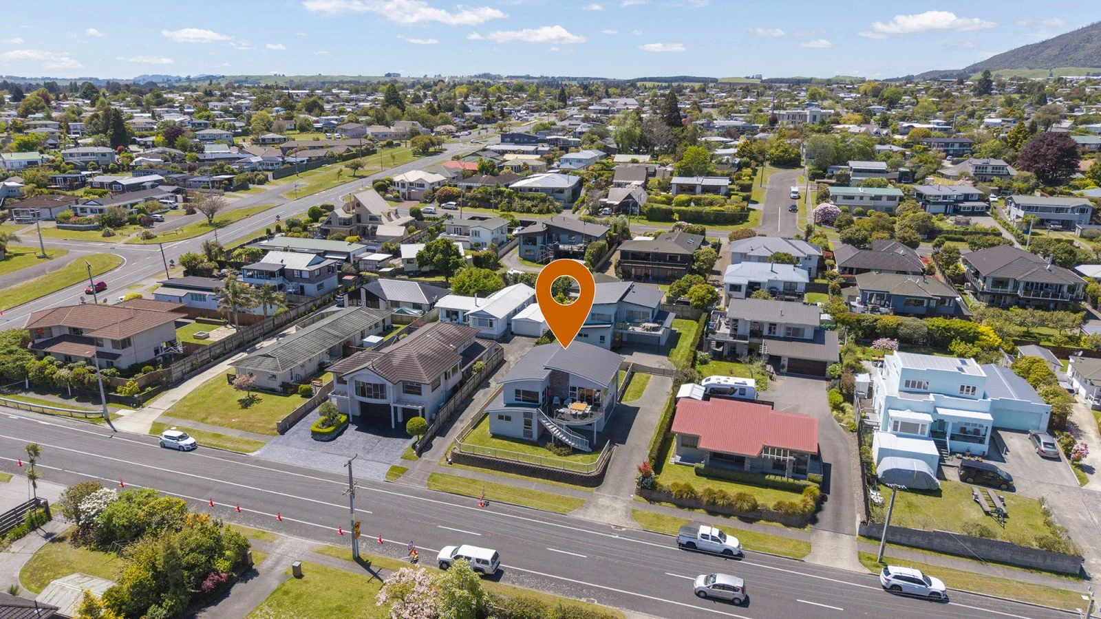 Aerial view of a suburban neighborhood with houses, trees, and streets, focusing on a specific house marked with an orange location pin.