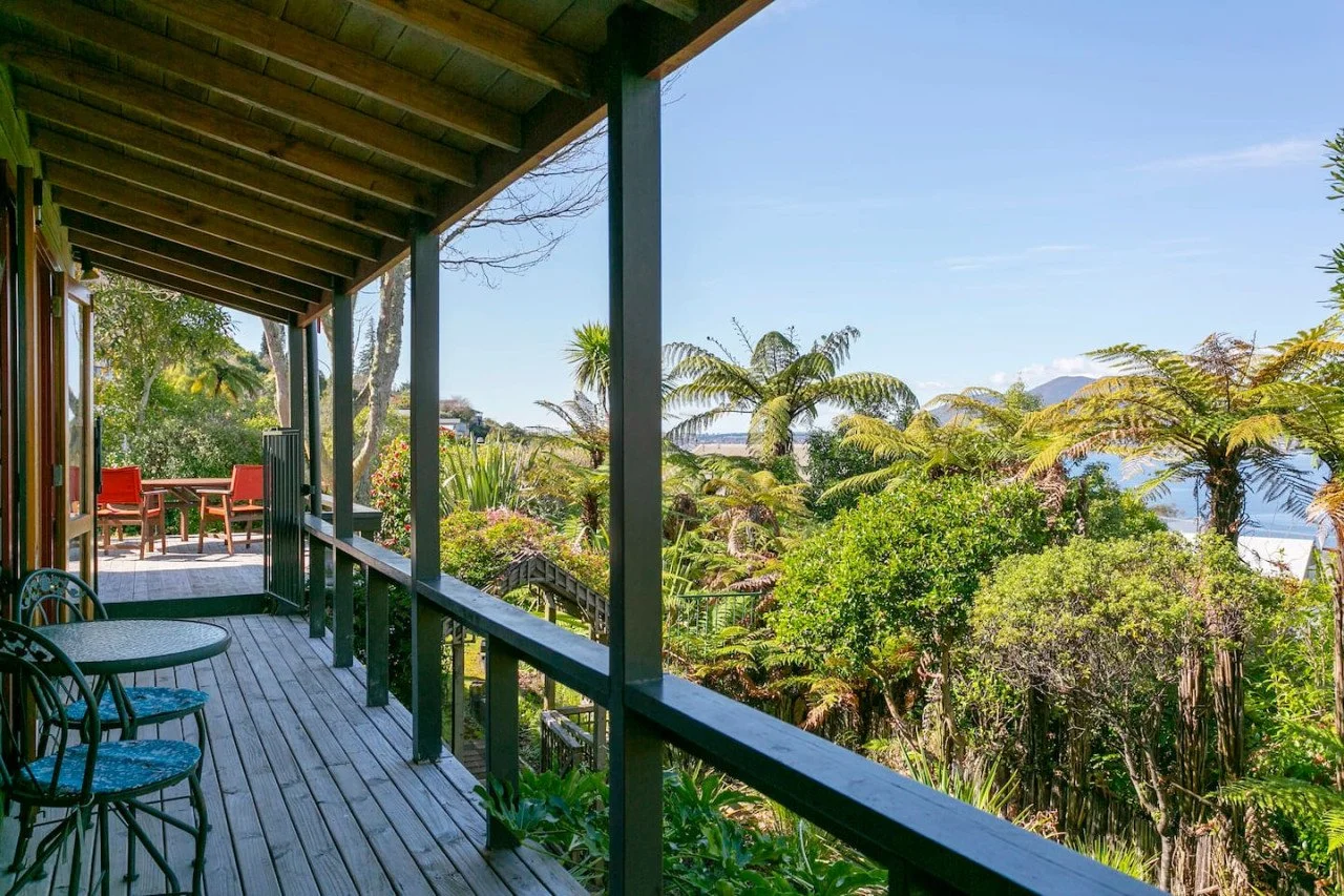 View from a wooden porch overlooking lush green tropical plants and trees, with a patio area in the background.
