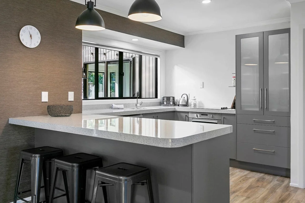 Modern kitchen with gray cabinetry, white countertops, a window above the sink, and a white wall with a clock.