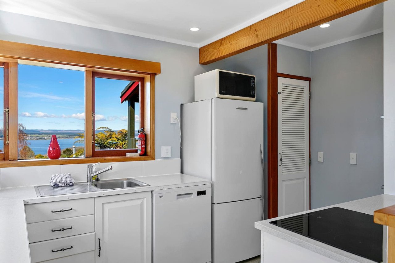 Kitchen with a window showing a lakeside view, white cabinets, a white refrigerator with a microwave on top, and a black electric stove.