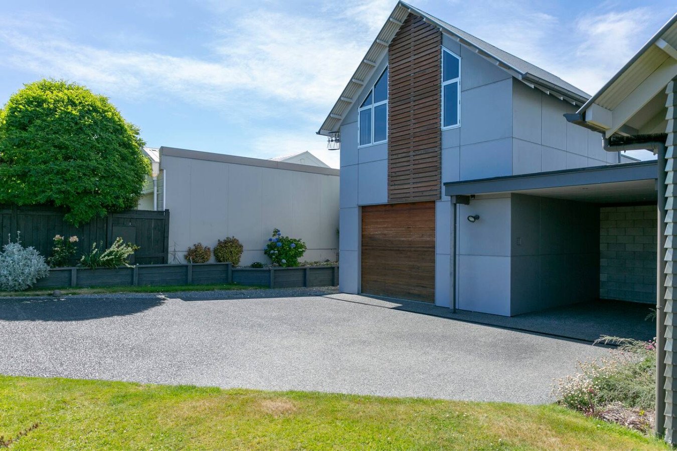 Modern residential house with a garage, landscaped garden, and a clear blue sky.