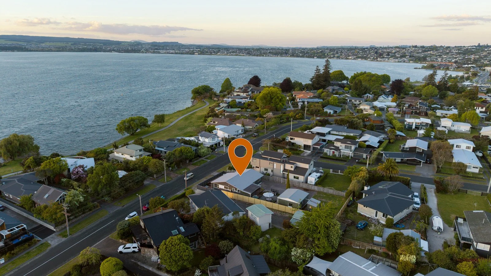 Aerial view of a residential neighborhood by a large body of water with houses, trees, and streets, during early evening.