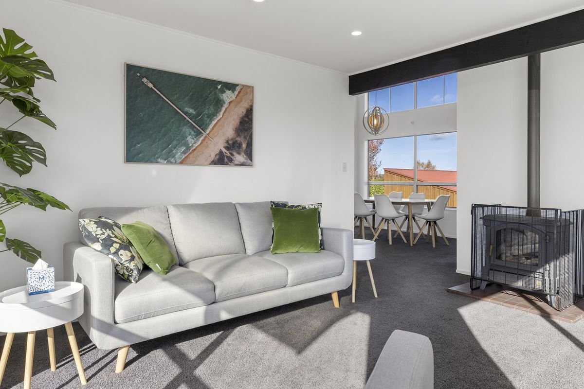 Living room with gray sofa, green pillows, wall art, fireplace, and dining area with white chairs near large window