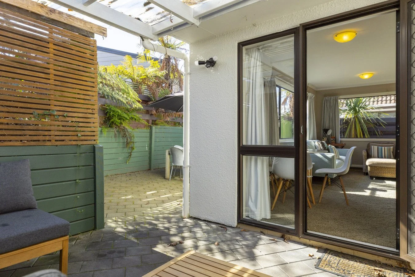 View of a patio with outdoor seating, a canopy, and a sliding glass door leading into a living room with white furniture and sunlight.