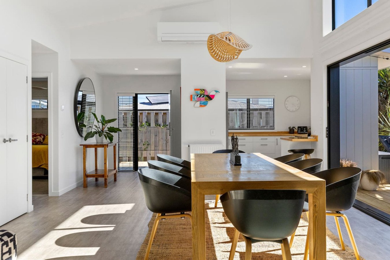 Modern dining room with wooden table, black chairs, and large sliding glass doors opening to an outdoor patio.