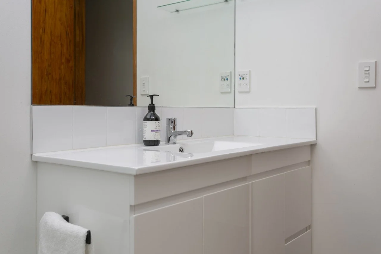 White bathroom sink with a soap dispenser, mirror, and wall switch on the wall.