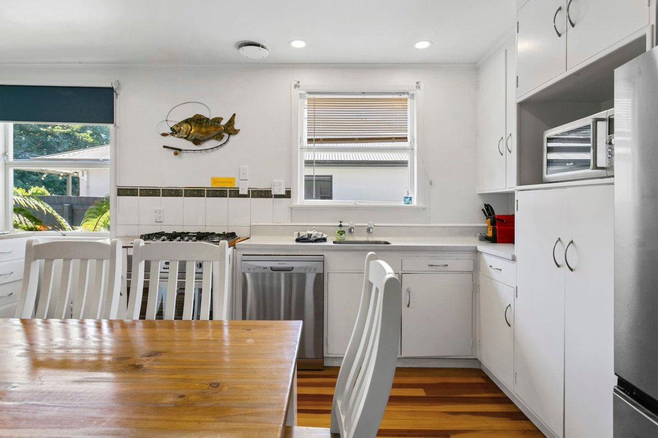 Kitchen with white cabinets, a wooden dining table with white chairs, a window with blinds, and a fish sculpture on the wall.