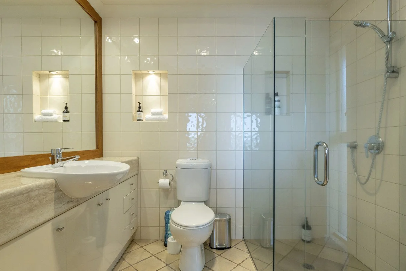 Bathroom with beige tiled walls and floor, a white toilet, a vanity with a sink and mirror, and a glass-enclosed shower area.