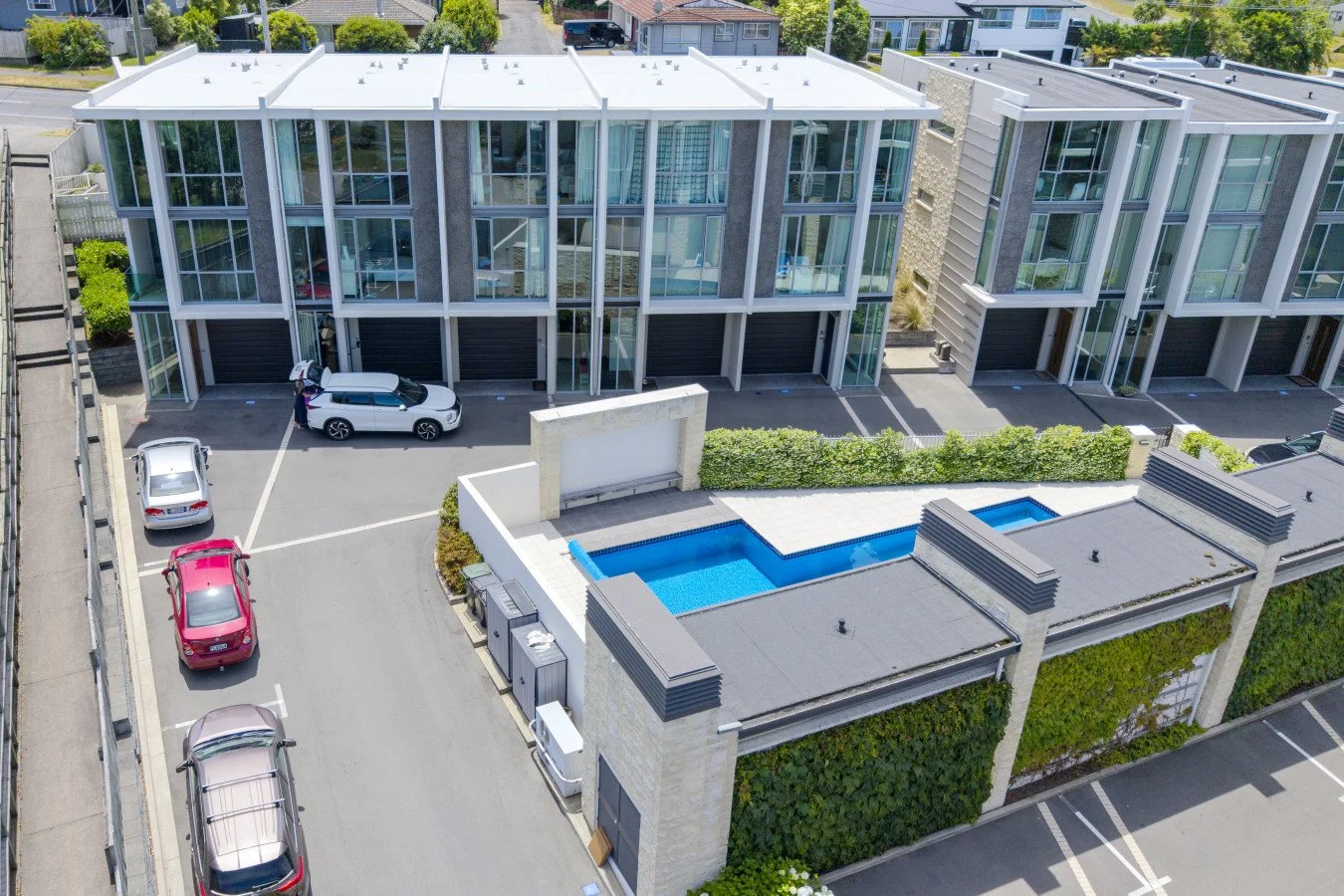 Aerial view of modern townhouse complex with glass exterior, parking spaces, and a swimming pool.