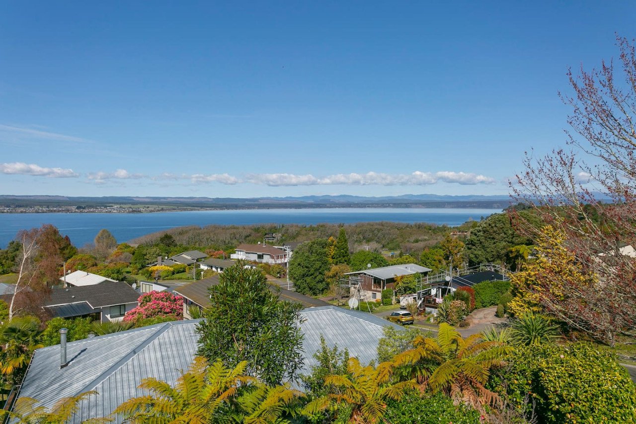 Scenic view of a residential area with houses, trees, and a large body of water in the background under a blue sky with clouds.
