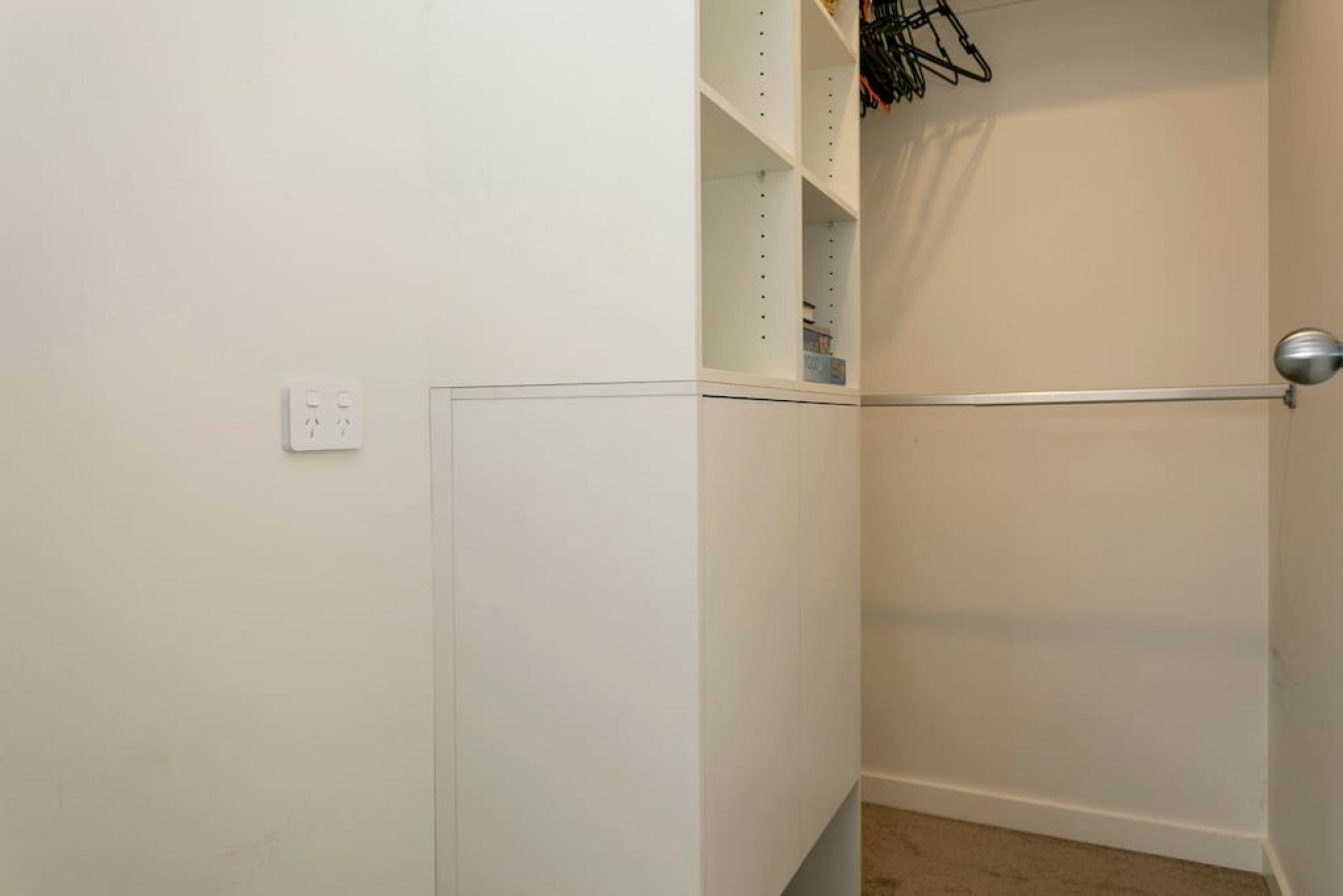 Empty walk-in closet with white shelving, hanging space, and beige carpet.