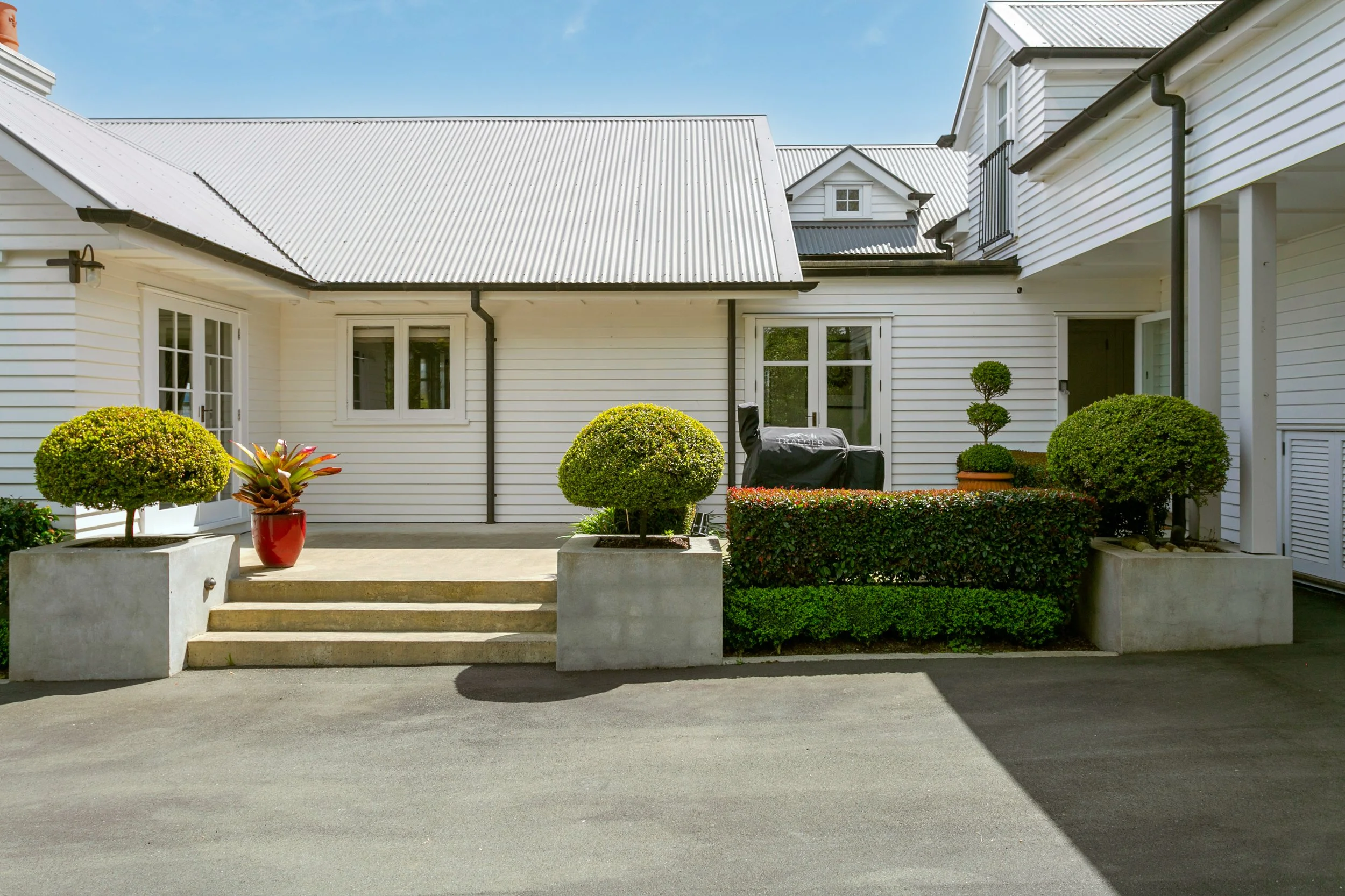 Front view of a white house with shrubs and potted plants near stairs and driveway