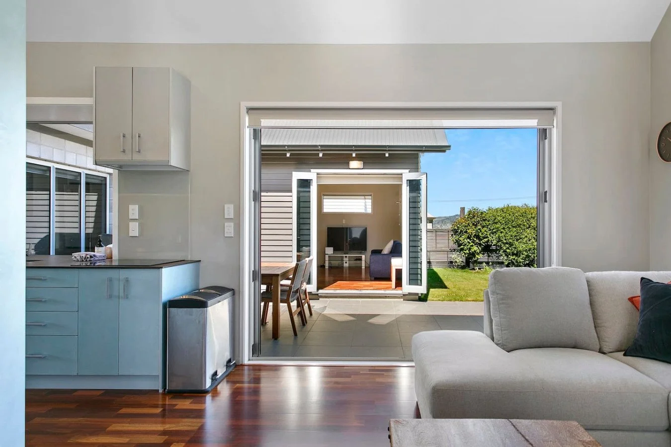 Living room with open patio doors showing outdoor patio and backyard garden with trees.