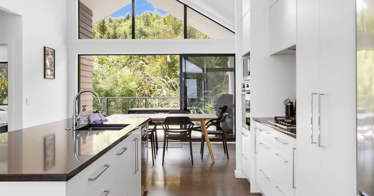 Modern kitchen with white cabinets, a black countertop, and large windows showing greenery outside